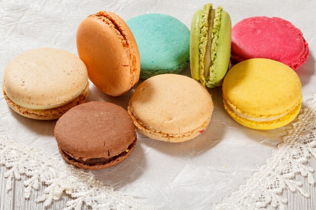 Gâteaux de macarons sucrés de différentes couleurs sur une serviette en soie avec un fond en bois