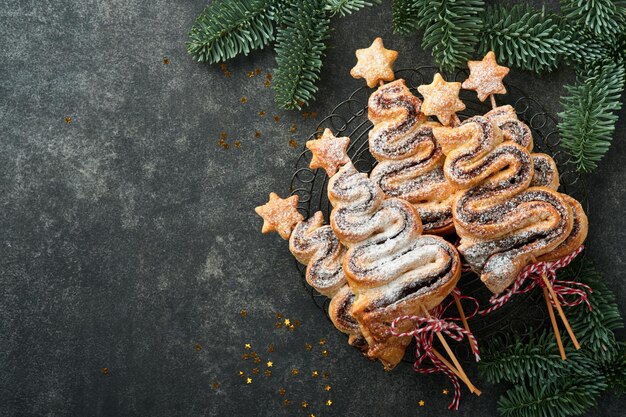 Gâteaux de pâte feuilletée en forme d'arbre de Noël avec poudre de sucre fourrée au chocolat et sucettes sur fond sombre ancien Apéritif de Noël Nouvel An Idée festive pour le dîner de Noël ou du Nouvel An