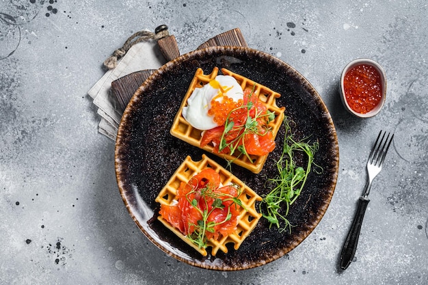 Gaufre belge avec fromage à la crème, tranches de saumon, œuf et caviar rouge. Fond gris. Vue de dessus.