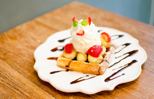 Photo gaufre avec garniture de crème glacée à la fraise et banane sur la table en bois