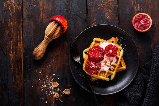 Gaufres au yogourt et sauce à l'orange sicilienne rouge sur la vieille surface en bois sombre. Vue de dessus.