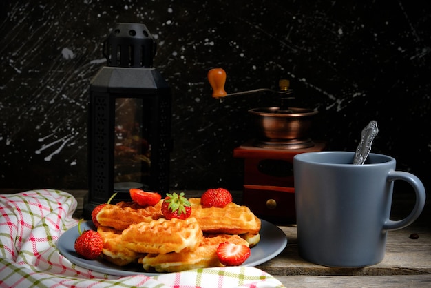 Gaufres aux fraises et au miel assiette de pâtisseries sucrées et tasse de café sur fond moulin à café et lampe à pétrole