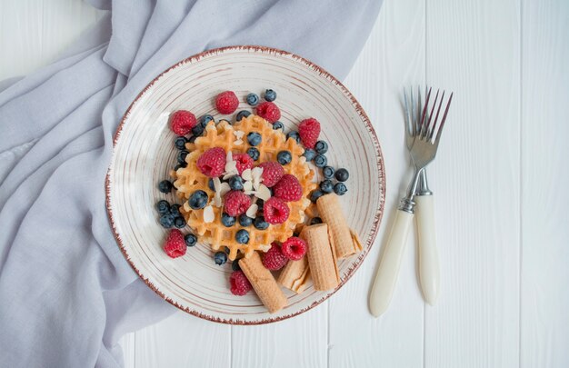 Gaufres aux framboises fraîches, bleuets pour le petit déjeuner. Gauffres belges. Fond en bois clair.