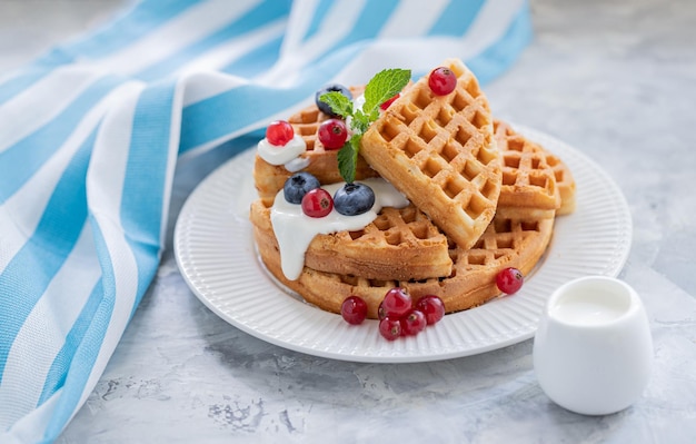 Gaufres aux myrtilles groseilles rouges coulées avec du yaourt sur une assiette en porcelaine blanche