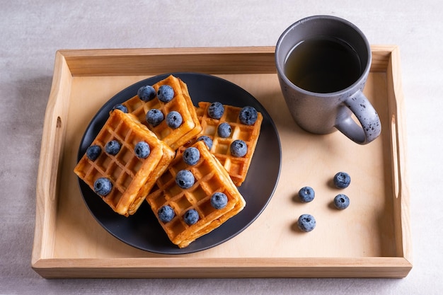 Gaufres aux myrtilles et tasse de thé sur un plateau en bois.