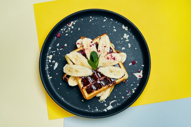 Gaufres belges au chocolat, bananes et amandes sur une plaque noire sur une surface colorée Pâtisseries sucrées appétissantes. Nourriture du petit déjeuner