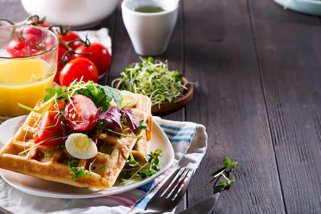 Gaufres belges avec avocat, oeufs, micro vert et tomates au jus d'orange sur une table en bois