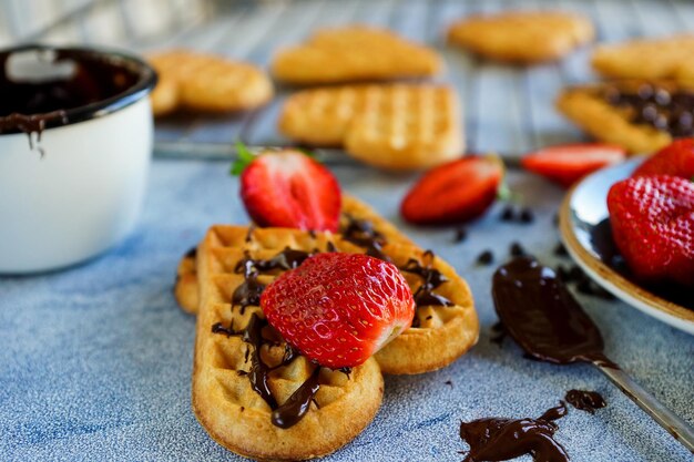 Gaufres belges en forme de coeurs avec fraises fraîches et garniture au chocolat sur table bleue