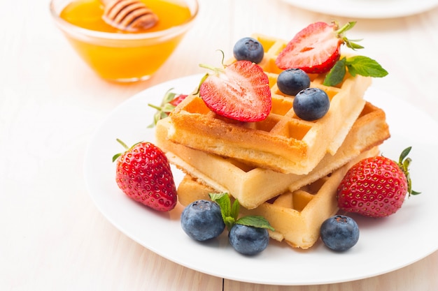 Gaufres belges fraîches faites maison avec du miel, des fraises et des myrtilles