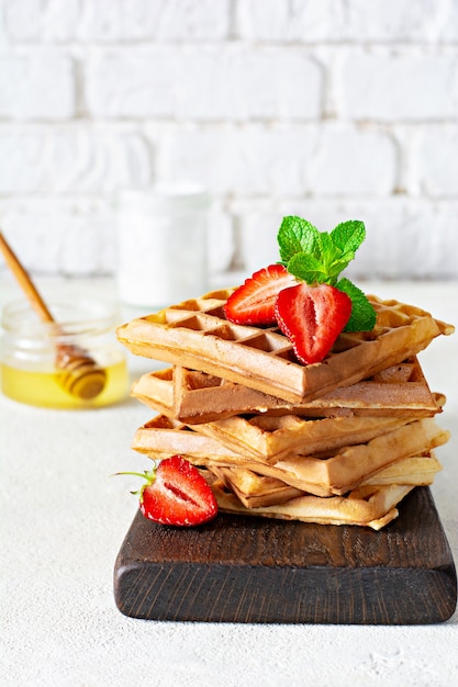 Gaufres Belges Fraîches Avec Des Fraises Mûres, De La Menthe Et Du Miel Pour Le Petit Déjeuner Sur Un Fond Clair.