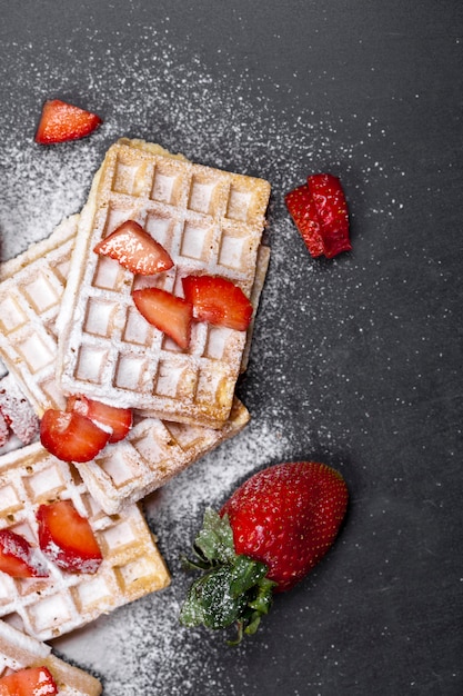 Gaufres belges avec des fraises et du sucre en poudre sur tableau noir.