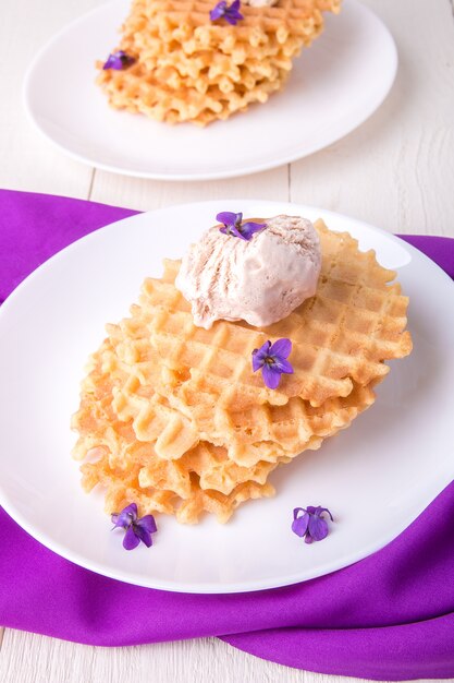 Gaufres belges avec de la glace sur une plaque blanche décorée de fleurs violettes. Vue de dessus.