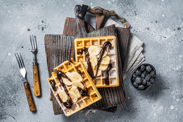 Gaufres belges traditionnelles avec banane fraîche et sauce au chocolat Fond gris Vue de dessus