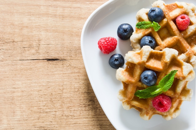 Gaufres belges traditionnelles avec des bleuets et des framboises sur l'espace de copie de table en bois