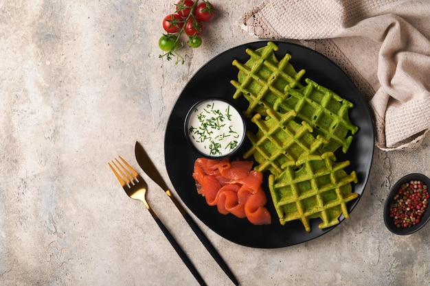 Gaufres belges vertes Epinards ou gaufres à l'ail des ours ou au pesto avec saumon rouge et sauce à la crème sur fond de table en béton gris Délicieux petit-déjeuner collation brunch Vue de dessus Maquette