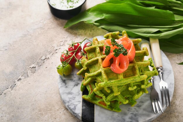 Gaufres belges vertes Epinards ou gaufres à l'ail sauvage ou au pesto avec saumon rouge et sauce à la crème sur fond de table en béton gris Délicieux petit-déjeuner snack-brunch Maquette Mise au point sélective