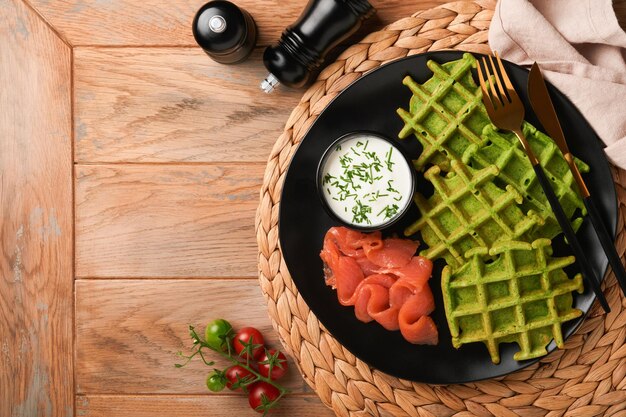 Gaufres belges vertes Épinards ou gaufres à l'ail des ours ou au pesto avec saumon rouge et sauce à la crème sur une plaque noire sur fond de bois rustique foncé Délicieux petit-déjeuner collation brunch Vue de dessus Maquette