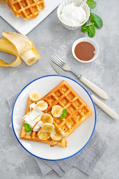 Gaufres à la crème fouettée à la banane et au caramel salé sur fond de béton gris