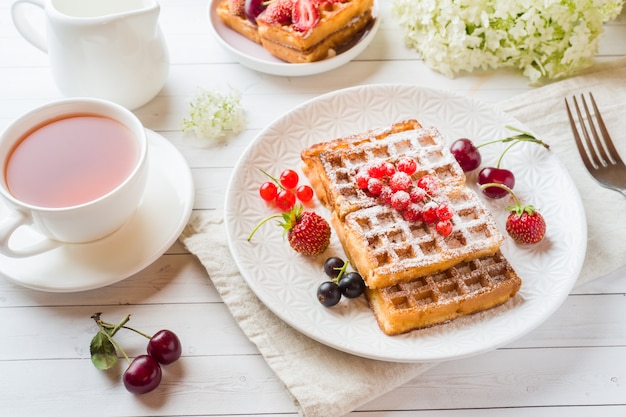 Gaufres faites maison avec des baies d'été sur une plaque. Une tasse de thé sur une table lumineuse. Mise au point sélective.