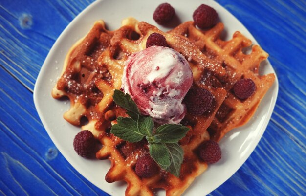 Gaufres avec glace à la framboise et framboises fraîches décorées de menthe sur fond de bois bleu