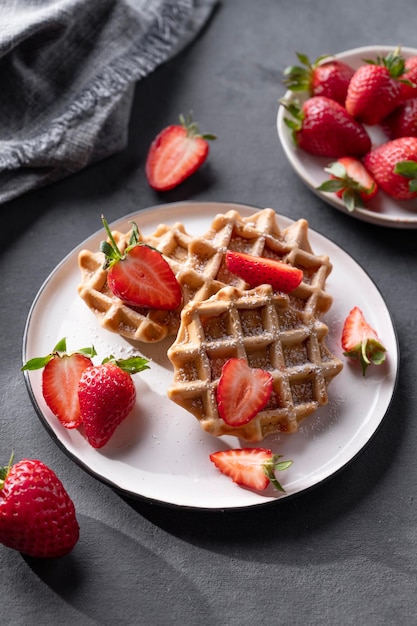 Gaufres molles faites maison avec des fraises fraîches et du sucre en poudre dans une assiette sur fond sombre Gaufres belges traditionnelles