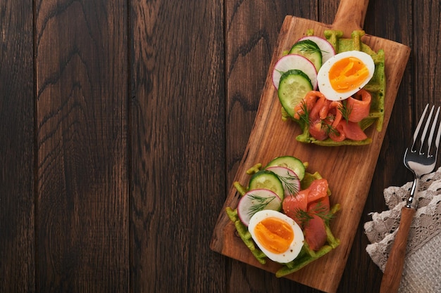 Gaufres salées Petit déjeuner gaufres vertes à l'ail des ours ou aux épinards avec oeuf tomate saumon sur une assiette en bois pour le petit-déjeuner sur un vieux fond en bois foncé Dîner léger déjeuner ou petit-déjeuner Vue de dessus Maquette