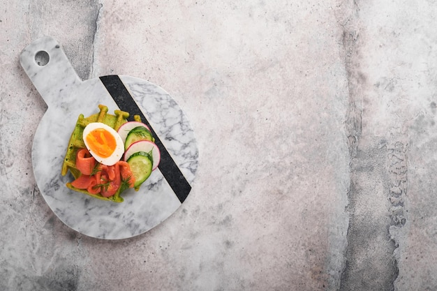 Gaufres salées Petit déjeuner gaufres vertes ail sauvage ou épinards avec oeuf tomate saumon sur assiette pour le petit déjeuner sur fond de table en béton gris Dîner léger déjeuner ou petit déjeuner Vue de dessus Maquette