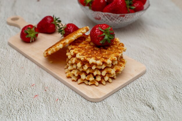 Gaufres servies avec des fraises sur une planche à découper blanche sur une table grise