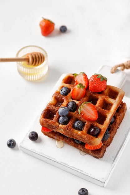 Gaufres sucrées aux baies, fraises, bleuets et miel Pile de gaufres sur fond blanc