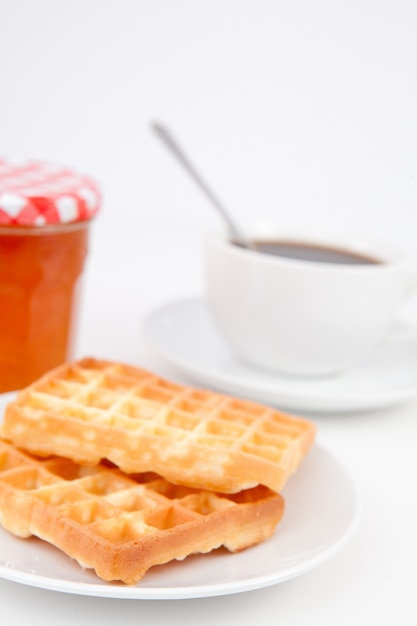 Gaufres et tasse de café avec une cuillère sur des assiettes et un pot de confiture