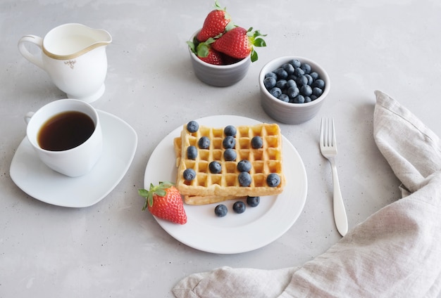 Gaufres viennoises ou belges fraîches avec des fraises et des bleuets et une tasse de café noir sur la table.