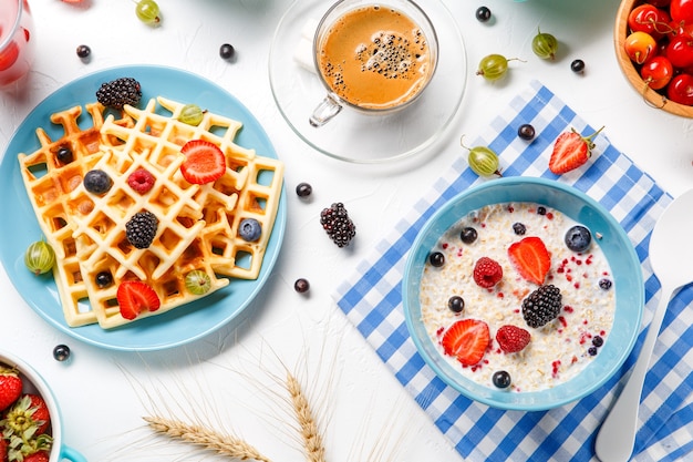 Gaufres viennoises, flocons d'avoine, café, framboises, fraises et groseilles sur une table blanche