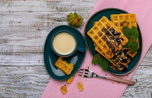 Gaufres viennoises avec glaçage au chocolat sur un plat bleu foncé sur un fond en bois clair une tasse de crème