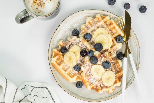 Gaufres viennoises maison aux myrtilles et à la banane et tasse de café sur fond clair