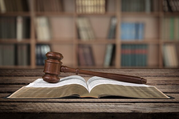 Gavel sur le livre de droit ouvert sur un bureau en bois au fond de la bibliothèque