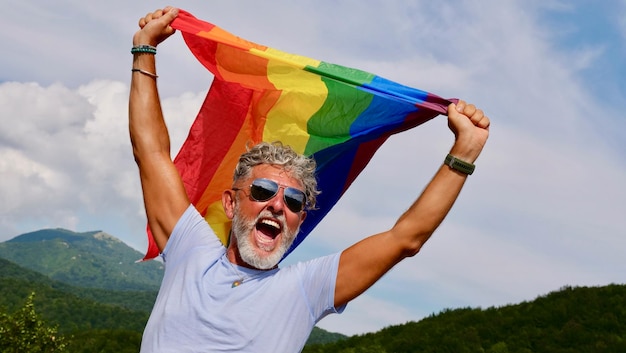 Gay grayhaired détient le drapeau LGBT contre un ciel