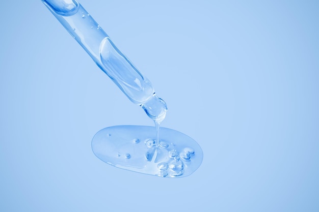 Le gel cosmétique transparent s'écoule d'une pipette directement sur le fond dans une grande goutte avec des bulles Sur un fond bleu Crème de gel de toner de toner d'acide hyaluronique Cosmétiques