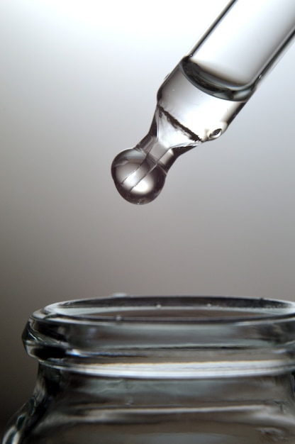 Gel transparent liquide ou pipette de sérum avec gouttes sur fond gris.