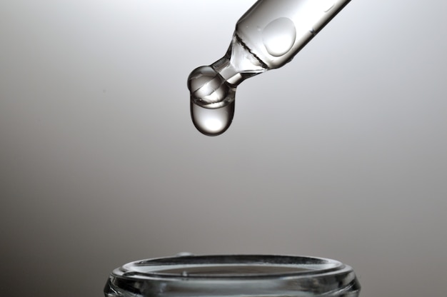 Gel transparent liquide ou pipette de sérum avec gouttes sur fond gris.