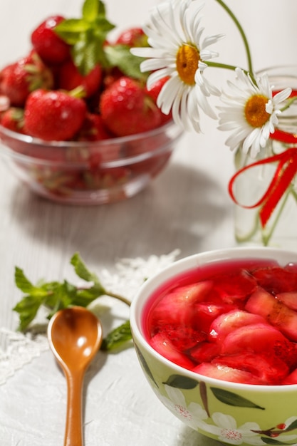 Gelée de cerises avec des morceaux de fraises dans le bol avec des fraises dans un bol et de la camomille en arrière-plan