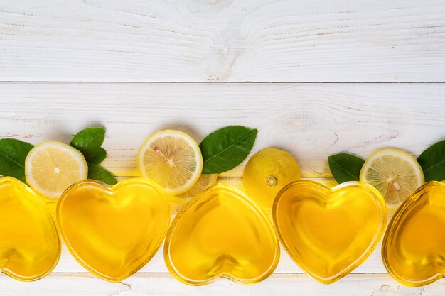 Gelée de citron jaune dans un verre en forme de coeur, tranches de feuilles de citron et de feuilles vertes sur du bois blanc