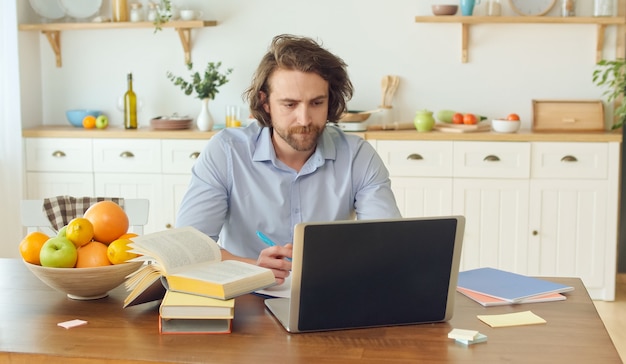 La génération d'aujourd'hui utilise l'étude à distance depuis la maison. Un homme séduisant utilise des livres et un ordinateur portable pour étudier ...