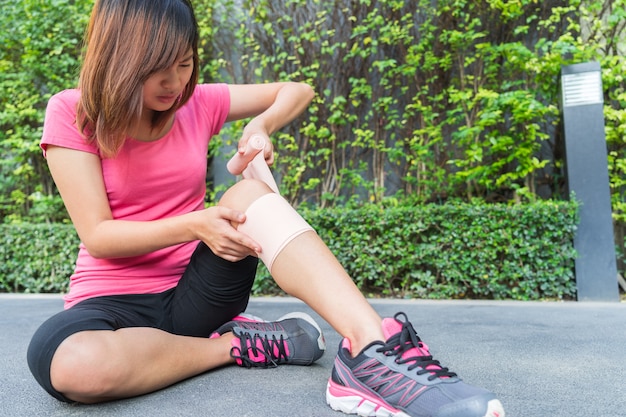 Genou de coureur de jeune femme étant appliqué bandage par lui-même dans le parc. blessure commune.