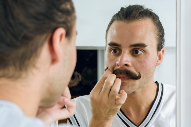 Genre personne latine non binaire devant le miroir fixant sa moustache