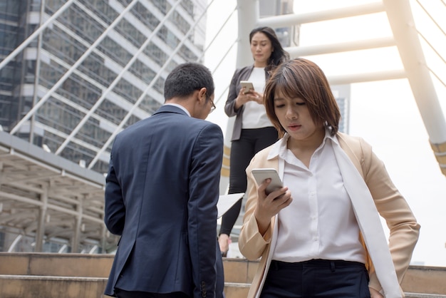 Gens d&#39;affaires asiatiques tenant un téléphone portable et marchant sur une passerelle moderne