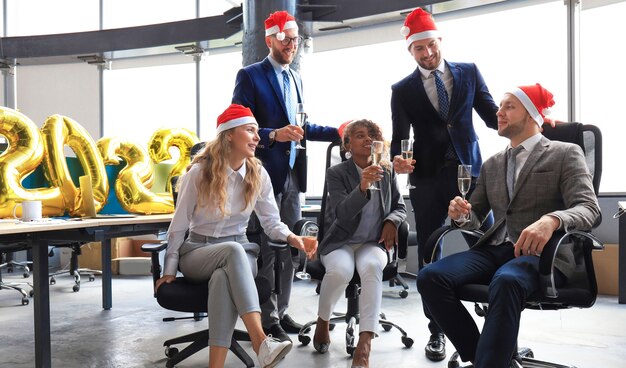 Les gens d'affaires célèbrent les vacances dans un bureau moderne en buvant du champagne et en s'amusant dans le coworking. Joyeux Noël et bonne année 2022.