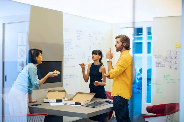 Gens d'affaires dans un bureau futuriste ayant une réunion, mangeant de la pizza