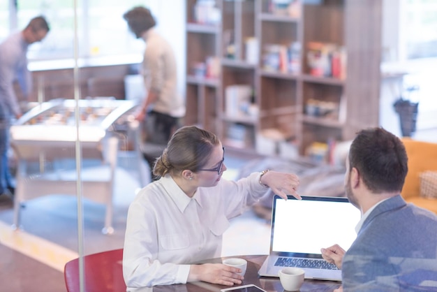 des gens d'affaires en démarrage utilisant un ordinateur portable se préparant pour la prochaine réunion tout en buvant du café et en discutant des idées dans un bureau créatif