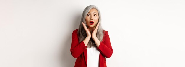 Gens d'affaires femme d'affaires senior asiatique en blazer rouge et maquillage haletant à la surprise de la cam