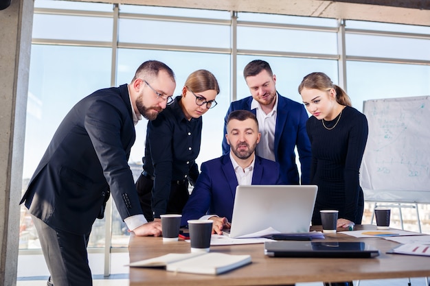 Des gens d'affaires heureux regardant la présentation d'un ordinateur portable, le succès au travail, assis dans un bureau moderne. Négociations en ligne réussies. Les hommes d'affaires partagent leurs connaissances